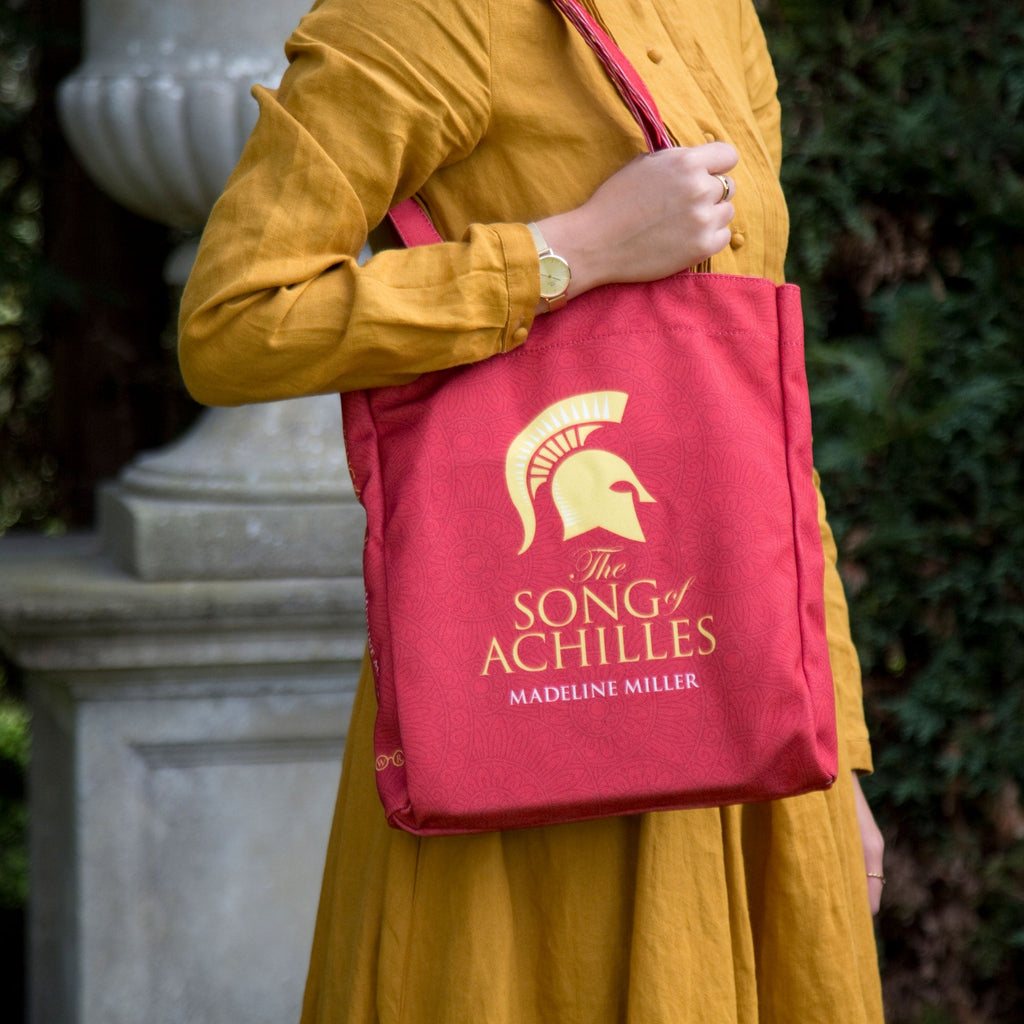 The Song of Achilles Red Tote Bag by Madeline Miller featuring Gold Trojan Helmet design, by Well Read Co. - Model with bag