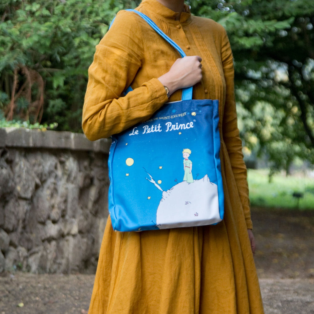 The Little Prince Blue Tote Bag by Antoine de Saint-Exupéry featuring Little Prince on his Home Planet design, by Well Read Co. - Model in Yellow Dress